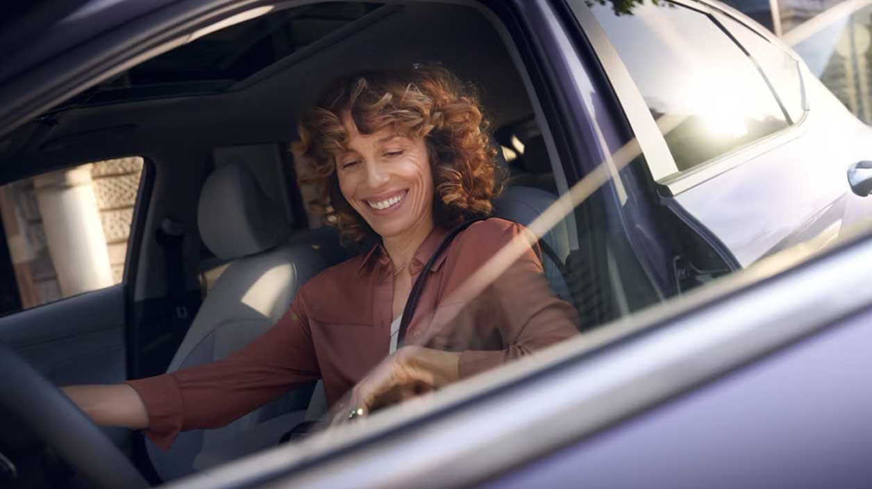 Une femme heureuse d'entrer dans sa voiture électrique garantie